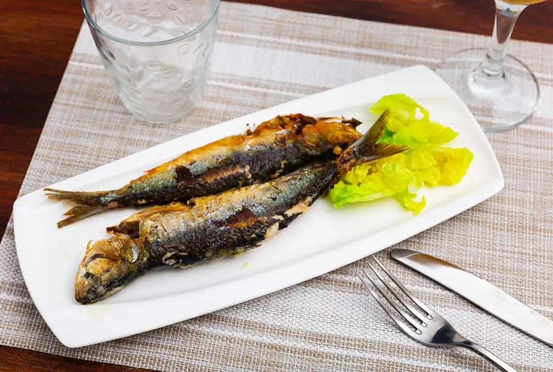Two grilled sardines served on a white plate with fresh lettuce leaves.